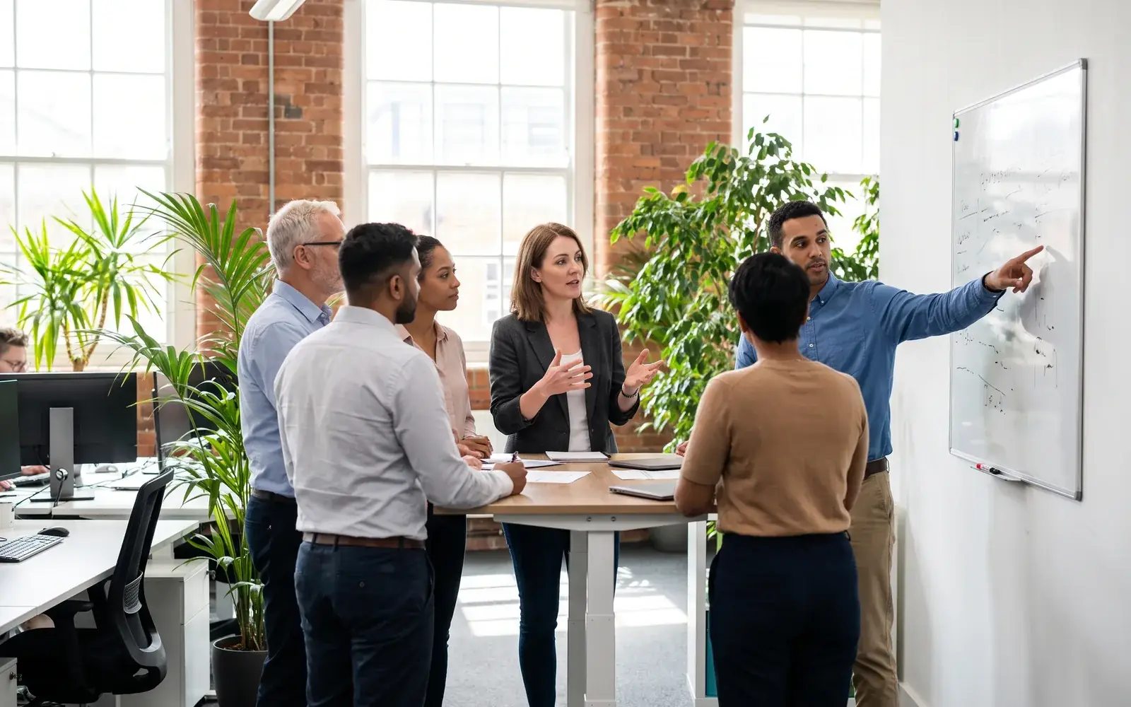 Colleagues meet on their feet beside a whiteboard in a bright open-plan scale-up office